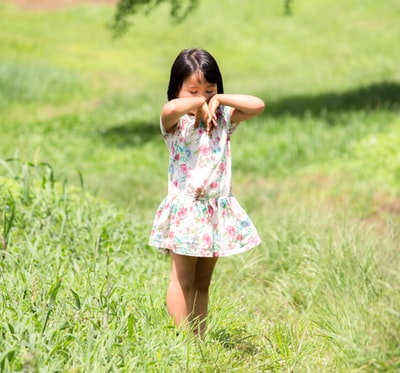 白天，穿着白粉色和绿色花朵连衣裙的女孩站在绿色的草地上